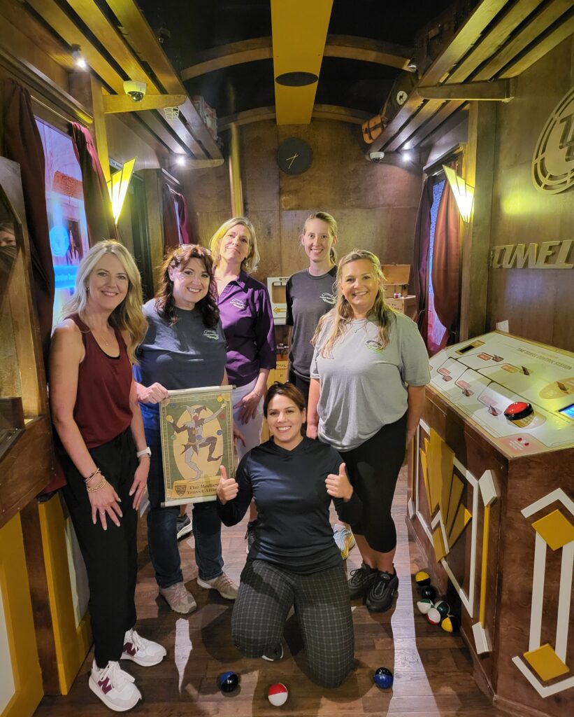 A group of six women posing in a cozy, warmly lit room with wooden decor.