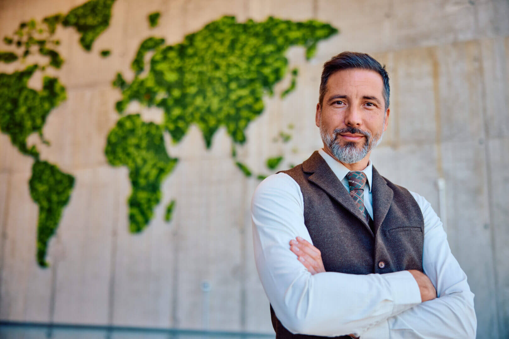 Confident man with folded arms stands before a green world map wall art.