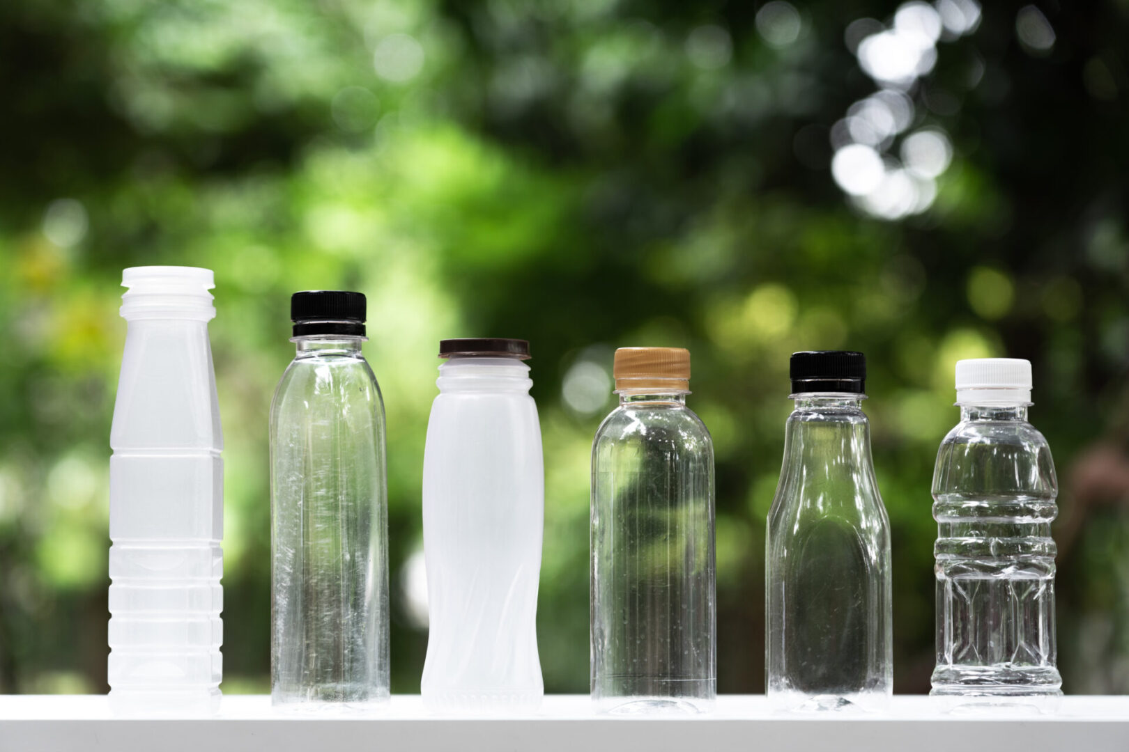 Many different shape bottles arrange into line with blur green garden background, re use container, eco friendly concept, copy space