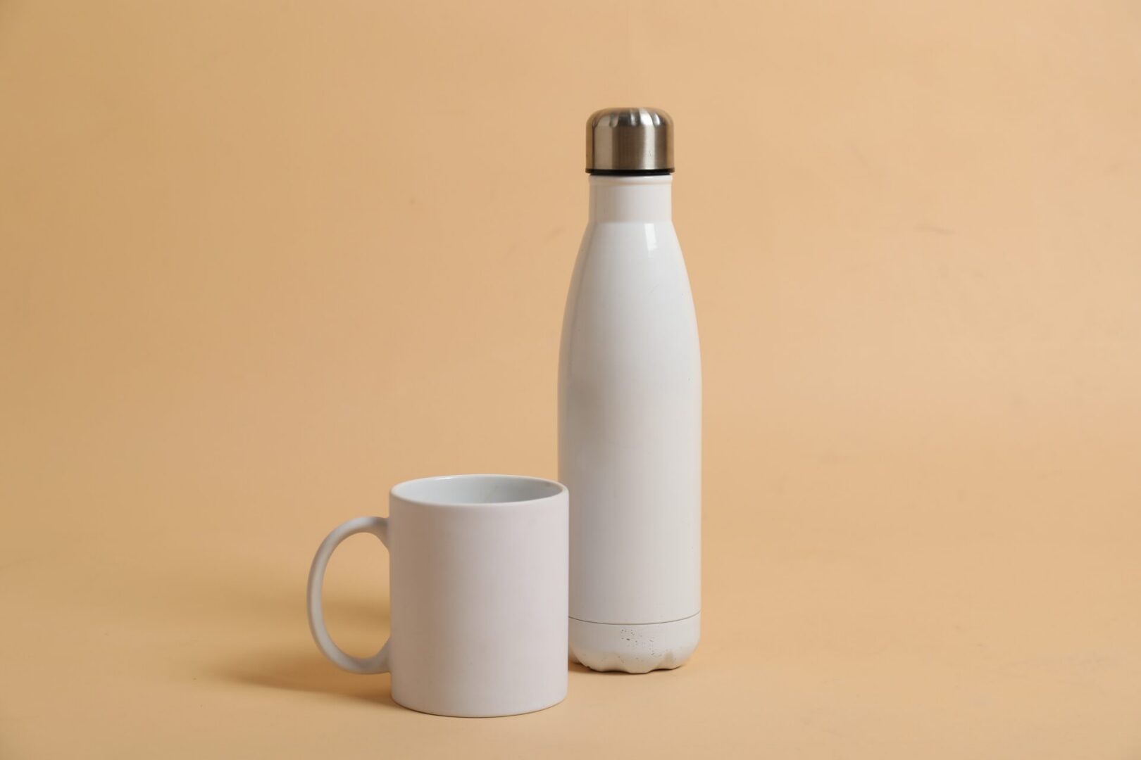 Blank mug and thermo bottle for branding on beige background. Mockup for design